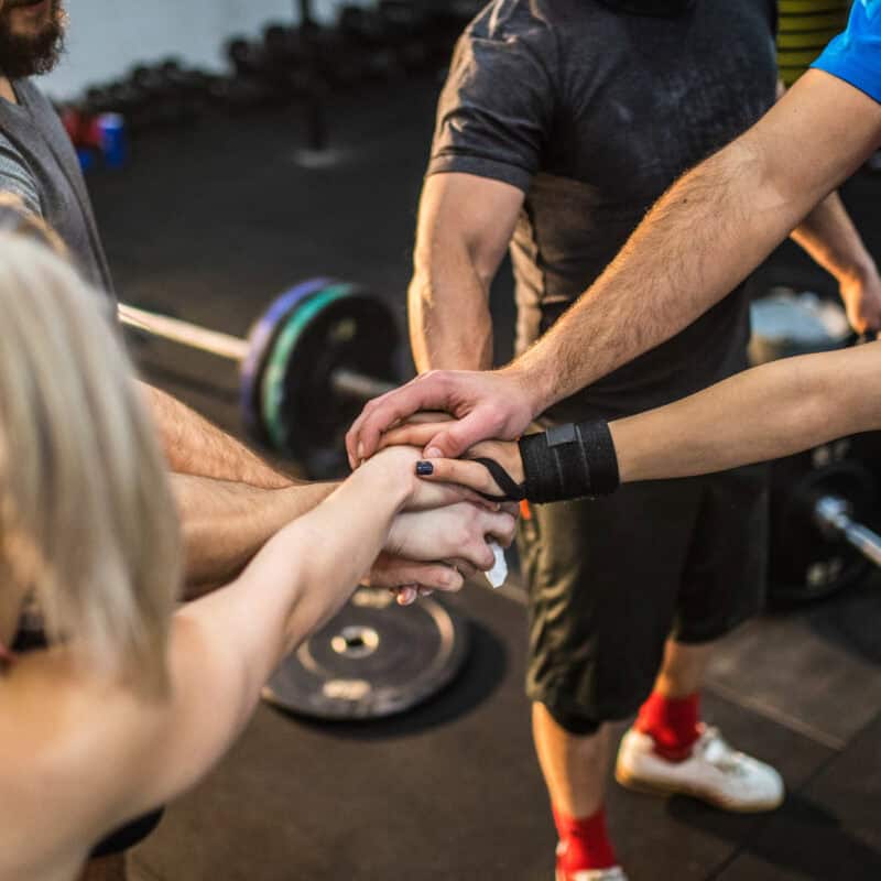People standing in a gym with their hands stacked together, highlighted by the seamless organisation enabled through club management software.