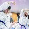 Karate students in white gis and blue belts practising stances in a dojo.