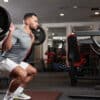 Gym owner practices barbell back squats in the mirror before sitting down to plan how he can grow his gym during the quieter summer months.