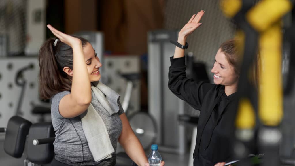 Two women smiling and giving each other a high-five at the gym, symbolising motivation, support, and community - key elements that help independent gyms stand out during the busy January rush.