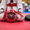 Martial artist in a red belt seated on a mat with protective gear and training equipment after joining a new dojo in January 2025.