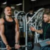 A member performs a bicep curl under the supervision of a personal trainer they booked to help them lift heavier.