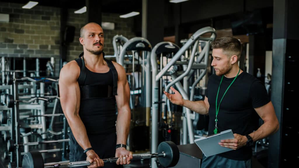 A member performs a bicep curl under the supervision of a personal trainer they booked to help them lift heavier.