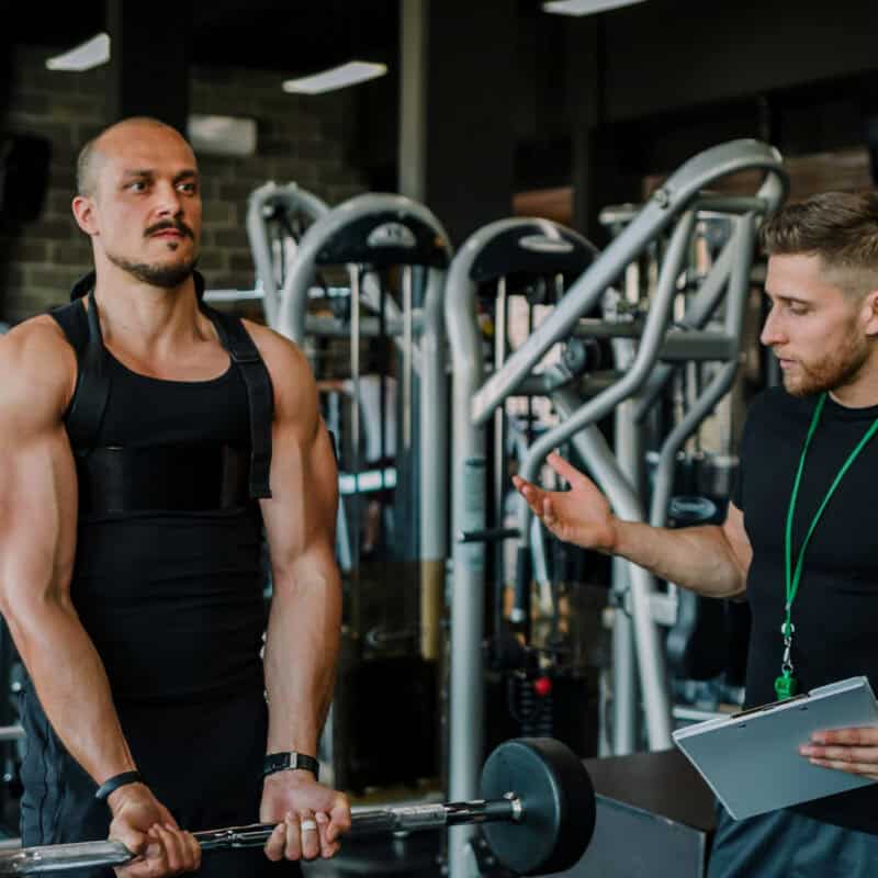 A member performs a bicep curl under the supervision of a personal trainer they booked to help them lift heavier.