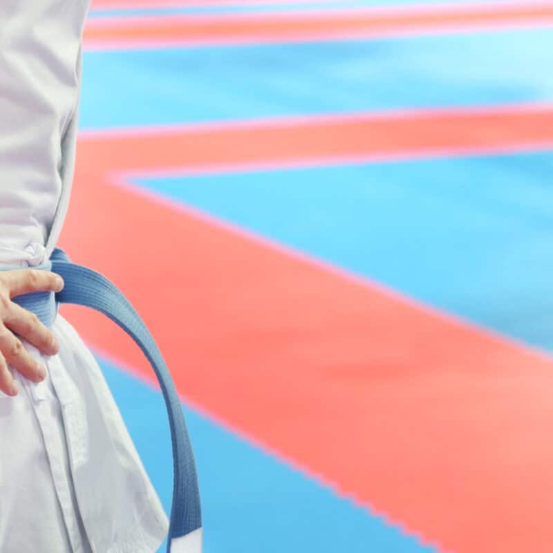 A martial artist wearing a blue belt stands confidently on the dojo floor, illustrating the life-changing impact of martial arts in a dojo environment.