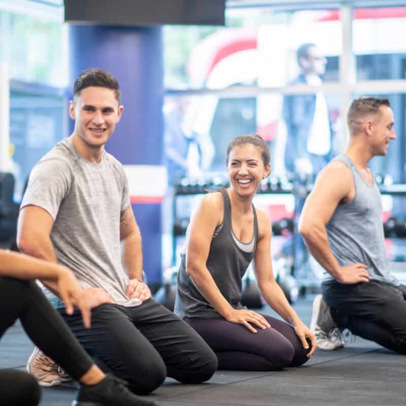 Group of gym members smiling and stretching together during a fitness class, showcasing community engagement and motivation; key elements of successful gym seasonal promotions.