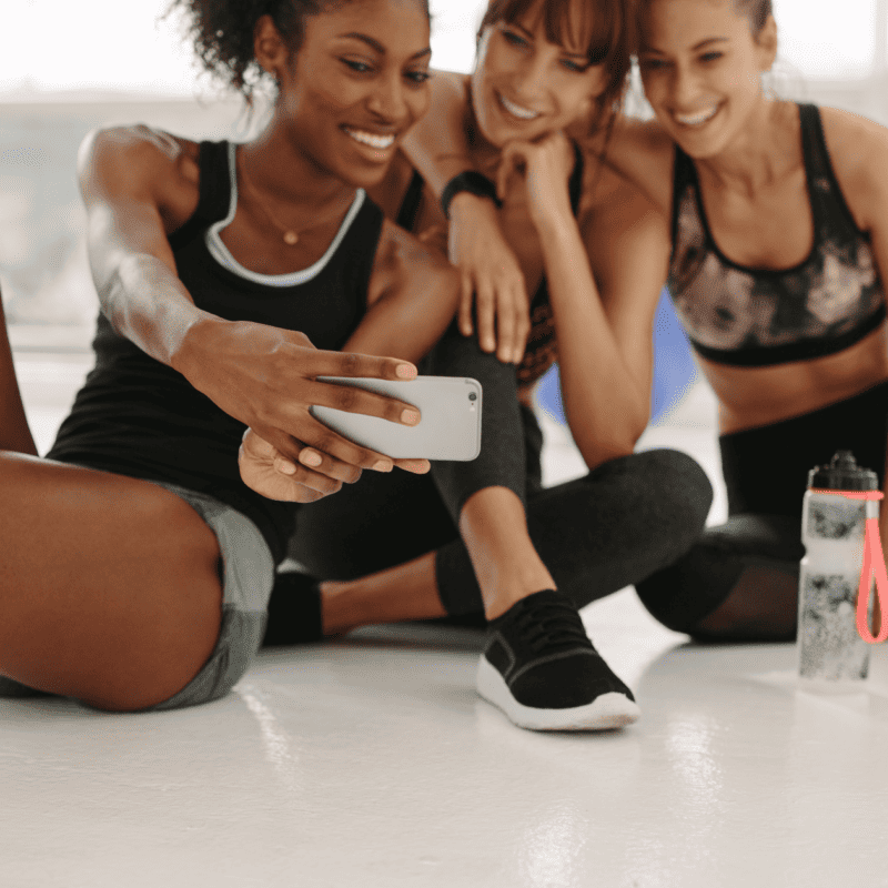 A group of women taking a selfie post-workout in a gym to show the achievement of their fitness goals on social media
