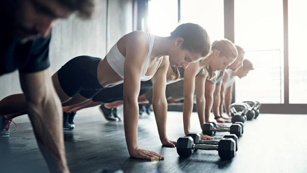 Group fitness class doing push-ups with dumbbells in the gym after a smooth member journey through the sales funnel.