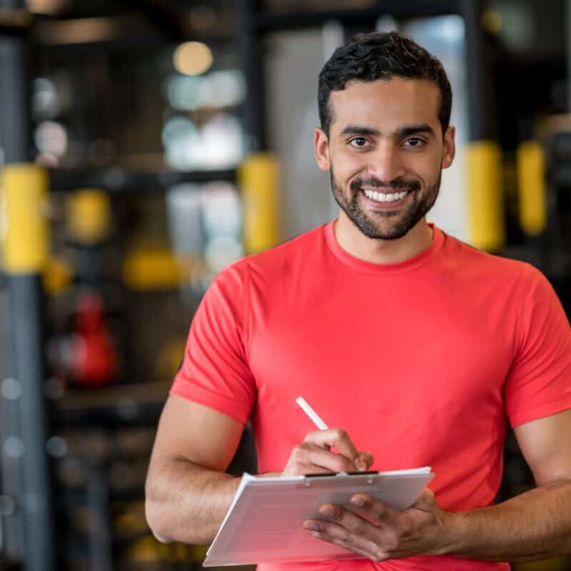 A smiling gym employee, smiling because he is confident that his members won't be freezing their memberships.