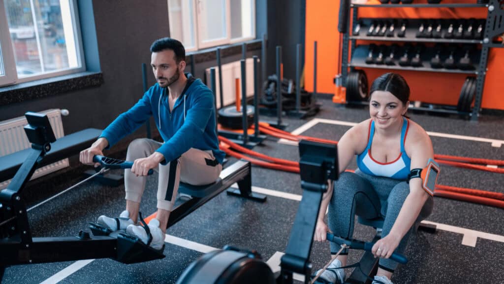 Two gym members using rowing machines side by side, after going from holding a day pass to buying a gym membership.