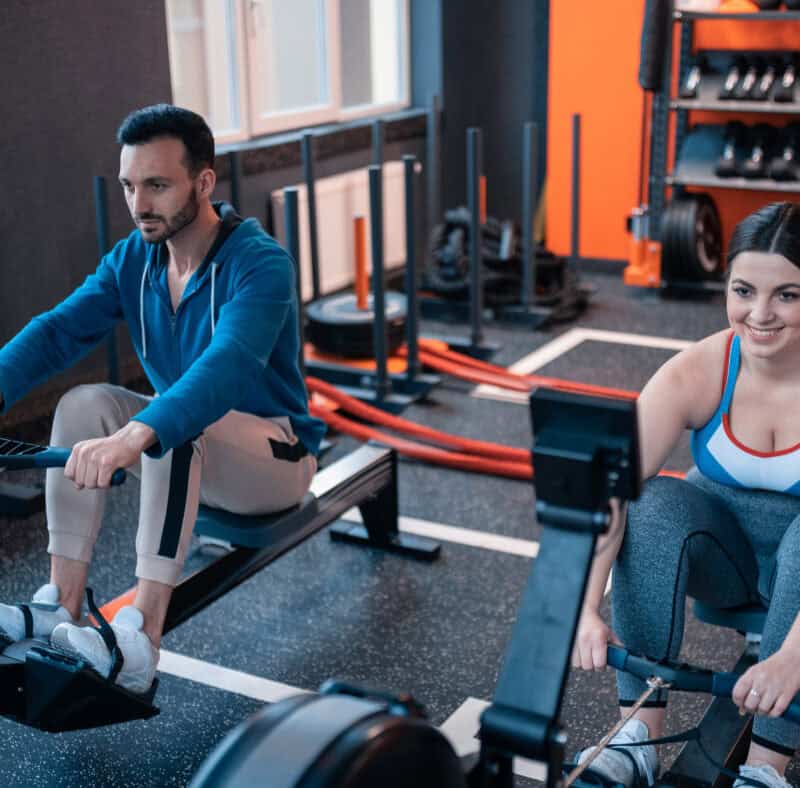 Two gym members using rowing machines side by side, after going from holding a day pass to buying a gym membership.