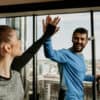 Two gym members smiling and high-fiving on cardio machines, highlighting positive member experience and community, a key factor when members choose a gym.
