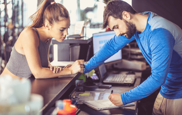 A male gym owner with a female member going through details to re-engage them to limit the chance of a frozen membership
